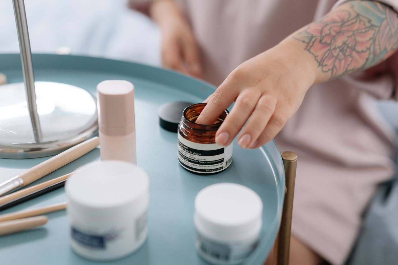 A close-up shot of a hand reaching for skincare creams on a blue tray indoors.